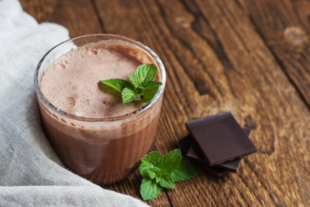 chocolate drink, smoothie in a glass glass with a sprig of mint on a linen napkin next to pieces of chocolate on a wooden background. dessert drinks. place for text - hot chocolate imagens e fotografias de stock
