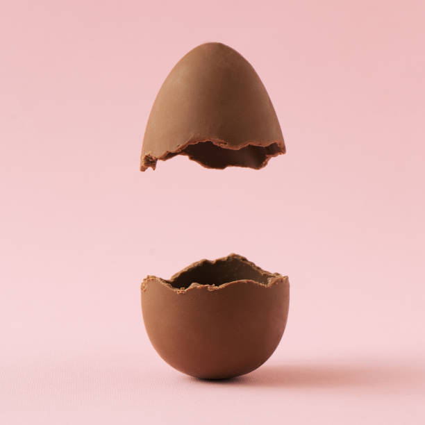 Chocolate Easter egg broken in half on pastel pink background with creative copy space. Minimal Easter holiday concept. easter egg stock pictures, royalty-free photos & images