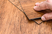 istock Choice of flooring. Renovation or construction concept. Close-up of a male hand holding a textured vinyl floor tile. Samples of laminate and vinyl floor tiles 1340566493