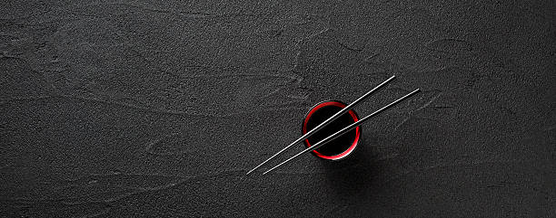 Chopsticks and bowl with soy sauce on black stone background stock photo