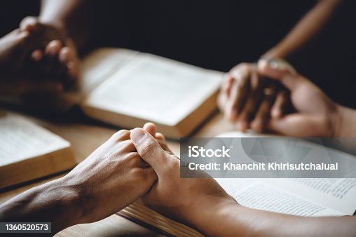 istock Christian group of people holding hands praying worship to believe and Bible on a wooden table for devotional or prayer meeting concept. 1360520573