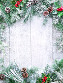 Christmas and New Year background with fir branches, holly and snowfall on wooden white board