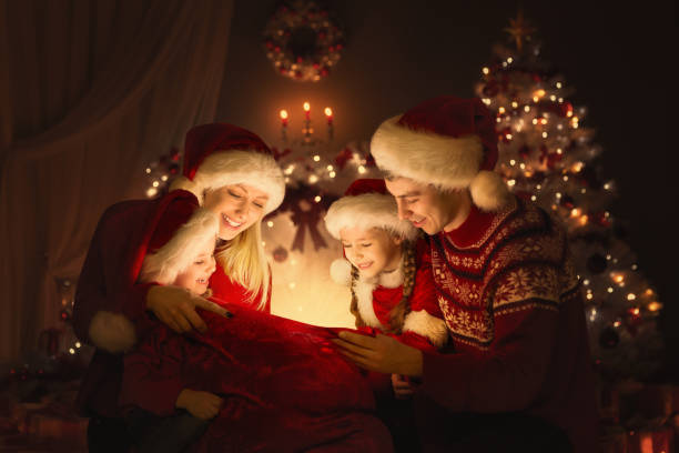 Christmas Family opening Santa Bag with Gifts. Happy Parents and Kids sitting in front of Decorated Xmas Fir Tree and looking at Magic Light. Winter Holiday Eve stock photo