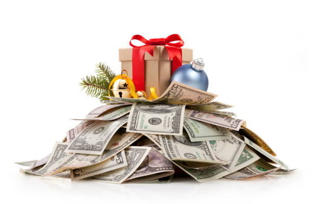 Christmas gift on top of a pile of dollar bills Christmas gift standing on a stack of US dollars isolated on white background. cost in italy stock pictures, royalty-free photos & images
