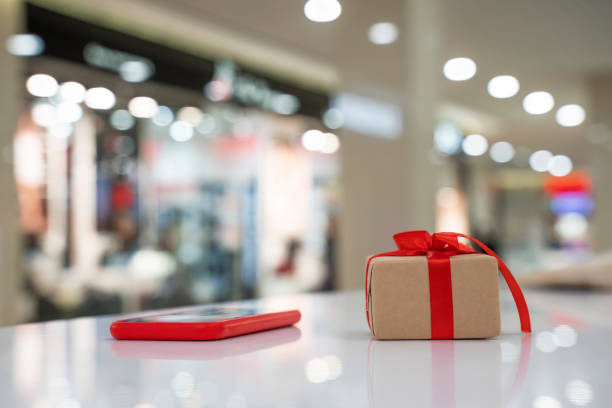 Christmas gift with red ribbon and Mobile phone. Christmas gift with red ribbon and Mobile phone.  Blurred bokeh background with red Smartphone and Gift Box. soft selective focus, copy space mall of america stock pictures, royalty-free photos & images