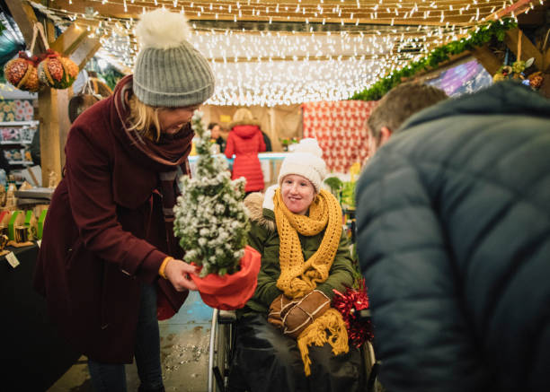 Christmas is the Time for Giving A front-view shot of a family buying gifts for their physically impaired daughter from a small business Christmas market stall in the city, they are wearing warm clothing on a cold December​ night. small business saturday stock pictures, royalty-free photos & images