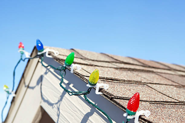 LED Christmas Lights on House Roof Peak Close-up detail portion of a long string of LED Christmas lights clipped to a house roof. The LEDs are housed within faceted plastic covers which replicate the look of incandescent bulbs. LEDs last longer and are much more efficient than conventional bulbs. christmas lights house stock pictures, royalty-free photos & images