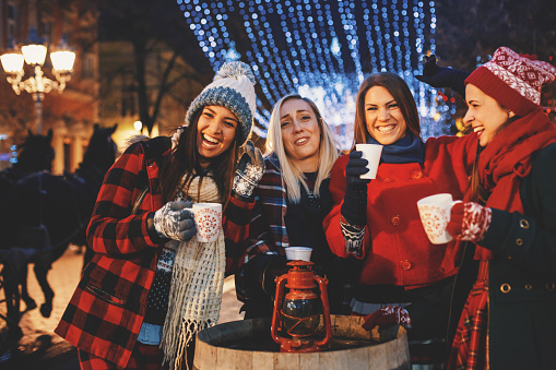Group of jolly friends cheering with hot drinks on a cold Christmas night.