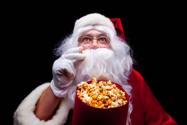 navidad. foto de santa claus con guantes en mano con un cubo rojo con las palomitas de maíz, sobre un fondo negro - navidad movie fotografías e imágenes de stock
