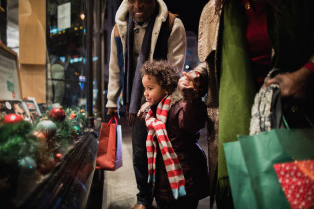 Christmas Shopping with Grandparents A side-view shot of two grandparents standing outside of a store window with their granddaughter in the city on a cold night, they are wearing warm clothing and holding hands. shopping mall photos stock pictures, royalty-free photos & images