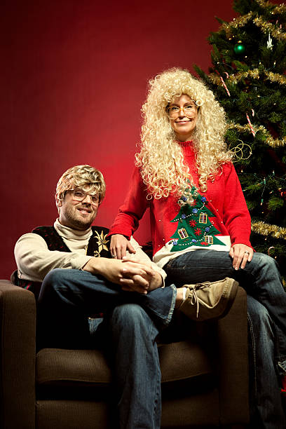 Christmas Sweater Eighties Couple Nerds of the 1980s, wearing classy knit Christmas sweaters with big, bad hair and glasses, pose for a picture in their living room next to their decorated Christmas tree looking awkward.  Happy Holidays.  Vertical with copy space. embarrassment photos stock pictures, royalty-free photos & images