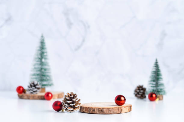 christmas tree with pine cone and decor xmas ball and empty wood log plate on white table and marble tile wall background.clean minimal simple style.holiday still life mockup to display design stock photo