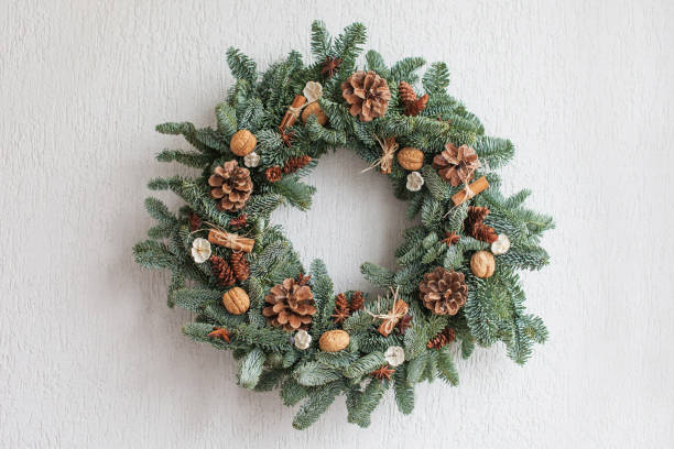 Christmas wreath made of natural fir branches  hanging on a white wall.  Wreath with natural ornaments: bumps, walnuts, cinnamon, cones. New year and winter holidays. Christmas decor stock photo
