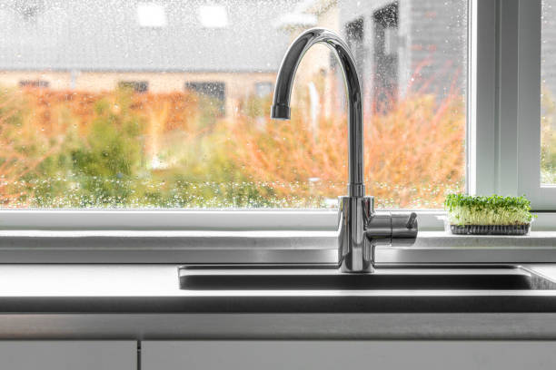 Chrome faucet by a kitchen sink with a wet window stock photo