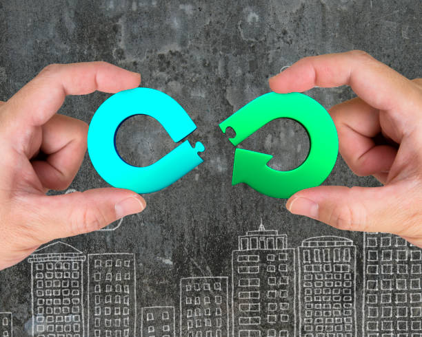 Circular economy concept. Circular economy concept. Two hands assembling arrow infinity recycling symbol of jigsaw puzzle pieces, on city buildings doodles background. circular economy stock pictures, royalty-free photos & images