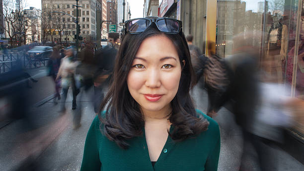 City girl portrait Beautiful young Asian woman standing on busy city sidewalk with people walking all around her. portrait close-up looking at camera. long exposure stock pictures, royalty-free photos & images