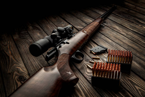 Classic bolt carbine .22lr with a wooden butt with a telescopic sight on a dark wooden background. Cartridges for a rifle next to a weapon. Hunter set. stock photo