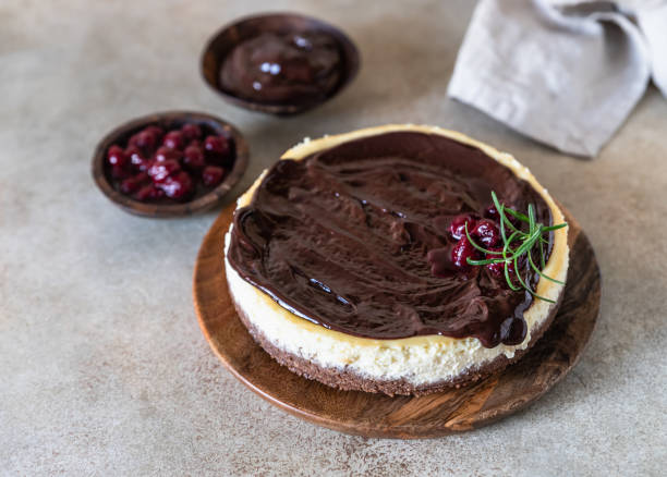 Classic creamy cheesecake with chocolate ganache, cherries and rosemary on concrete background. Popular festive dessert. stock photo