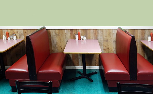 Classic diner interior with red leather booths, pink tables and blank green wall with copy space.
