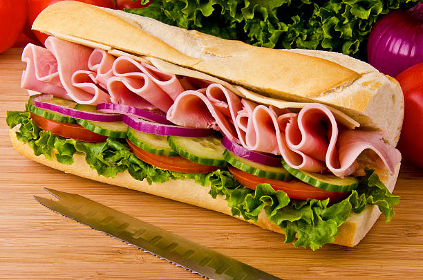 Classic ham, cheese and salad submarine sandwich Sub sandwich on a cutting board. Tomatoes, onion and lettuce background. sandwich photos stock pictures, royalty-free photos & images