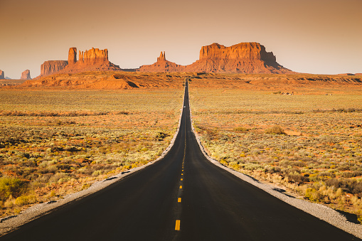 Classic panorama view of historic U.S. Route 163 running through famous Monument Valley in beautiful golden evening light at sunset in summer, Utah, USA