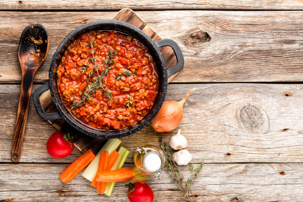 classic italian bolognese sauce stewed in cauldron with ingredients on wooden table, top view, culinary background with space for text stock photo