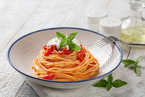 Classic italian pasta spaghetti with tomato sauce, stracciatella cheese and basil leaves. On white wooden table. stock photo