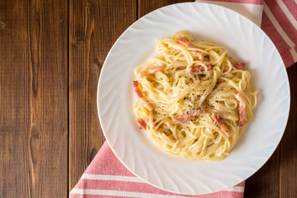 Classic pasta carbonara. Spaghetti with bacon, egg yolk and parmesan cheese on white plate on dark wooden background. stock photo