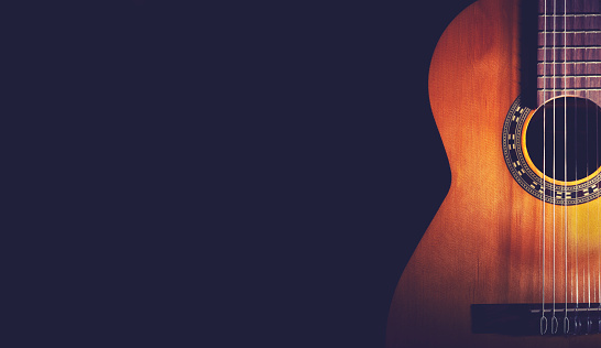 Classical Guitar on a dark wood background. Guitar wood is light brown with nice grain. Guitar has nylon strings with a pattern around the sound hole.