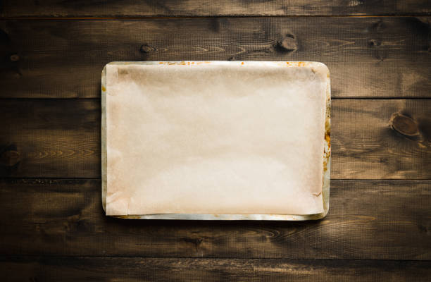 Clean baking sheet with cooking paper on the rustic background. Selective focus. Clean baking sheet with cooking paper on the rustic background. Selective focus. Shot from above. baking sheet stock pictures, royalty-free photos & images