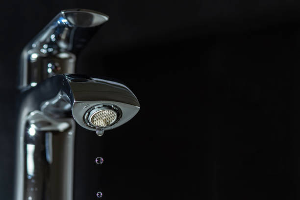 Clean water is dripping from the faucet on a black stock photo