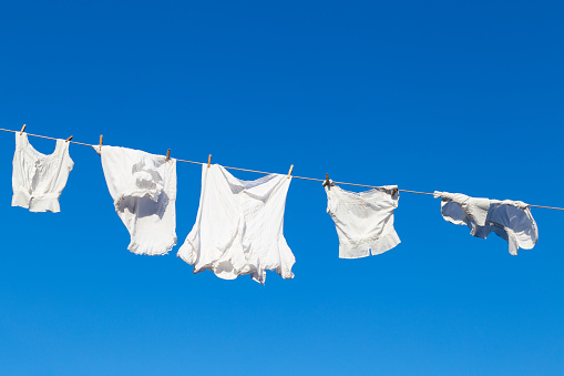 Clean white laundry hanging to dry on a rope against the blue sky during a beautiful sunny day
