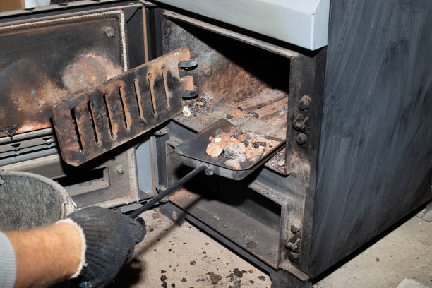 Cleaning the solid fuel boiler from the remains of firewood and coal. Boiler with an open damper. Heating efficiency in the house stock photo
