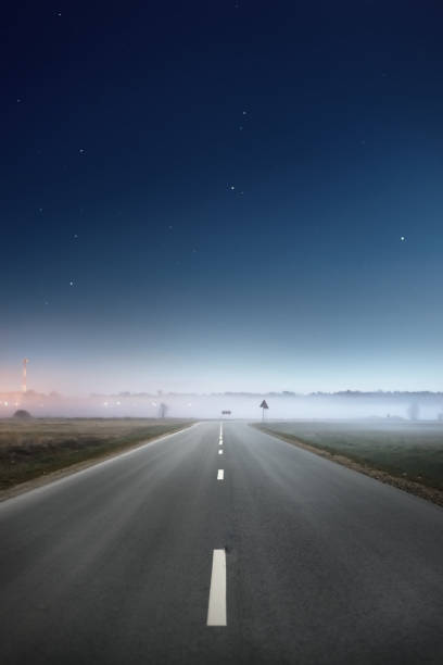 Clear blue starry sky and fog above the empty highway at night. Atmospheric landscape. Idyllic rural scene. Concept image, driving, transportation, road trip, adventure, freedom stock photo
