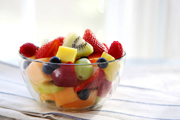 Clear bowl of sliced summer fruits on a dish towel fruit salad fruit salad stock pictures, royalty-free photos & images