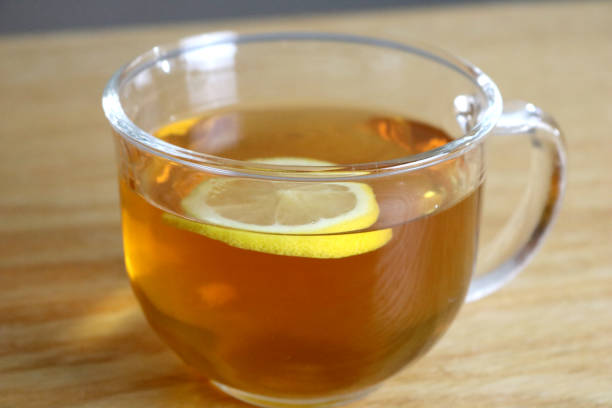 Clear Glass Cup of Amber Colored Tea with Lemon Slice Floating Close-Up stock photo