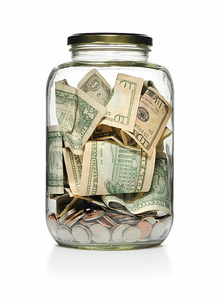 a clear glass jar filled with cash and coins  - glazen pot stockfoto's en -beelden