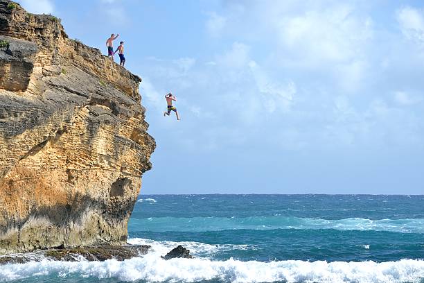Cliff Diving in Kauai, Hawaii USA A young man in his 20s is cliff diving in Kauai, while his friends cheer him on. cliff jumping stock pictures, royalty-free photos & images