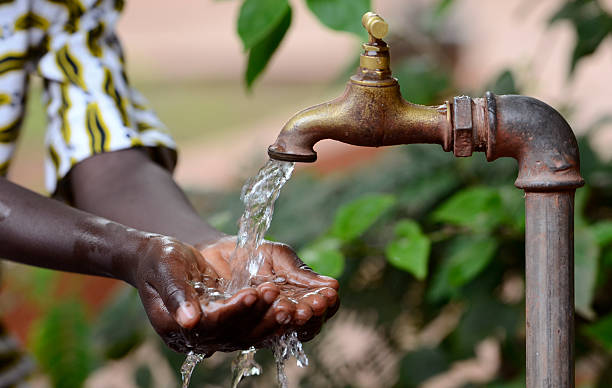 Climate Change Symbol: Handful Of Water Scarsity for Africa Symbol Hand of an African black boy with water pouring from a tap. Water scarcity or lack of safe drinking water is one of the world's leading problems affecting more than 1 billion people globally, meaning that one in every six people lacks access to safe drinking water. This affects people and especially children in Africa. developing countries stock pictures, royalty-free photos & images