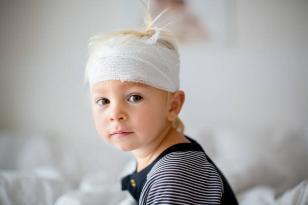 Close portrait of little toddler boy with head injury, sitting in bed, tired stock photo