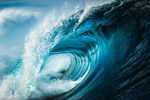 Close up detail of powerful teal blue wave breaking in open ocean on a bright sunny afternoon
