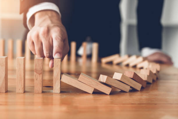 Close up finger businessman stopping wooden block from falling in the line of domino with risk concept. stock photo