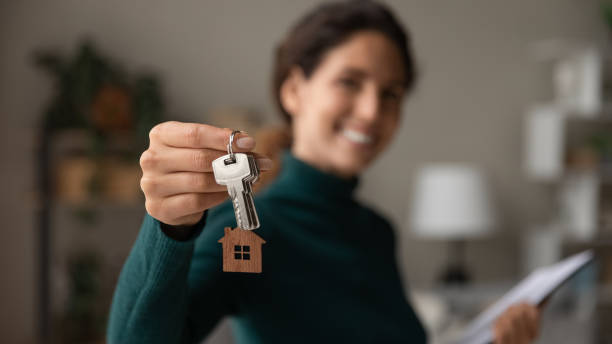 close up focus on keys, smiling woman real estate agent selling apartment - makelaar stockfoto's en -beelden