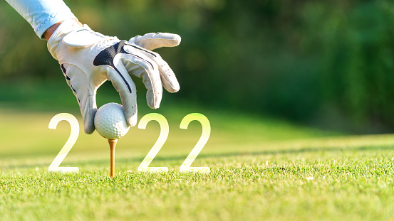 Close up hand Golfer woman putting golf ball for Happy New Year 2022 on the green golf for new healthy.  copy space. Healthy and Holiday Concept.