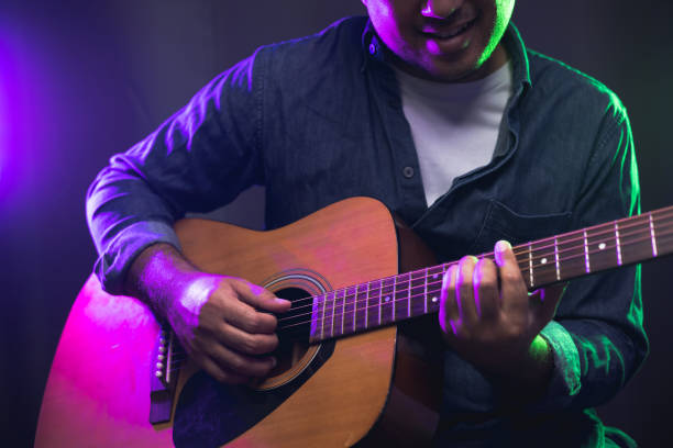 Close up hands young man playing acoustic guitar on stage live in concert. With neon light. Young man practicing music and solo guitar on the show. stock photo