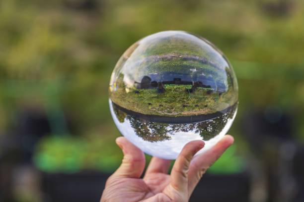 Close up macro view of hand holding crystal ball with inverted image of green natural landscape Close up macro view of hand holding crystal ball with inverted image of green natural landscape reentry stock pictures, royalty-free photos & images