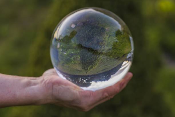 Close up macro view of hand holding crystal ball with inverted image of green natural landscape Close up macro view of hand holding crystal ball with inverted image of green natural landscape reentry stock pictures, royalty-free photos & images