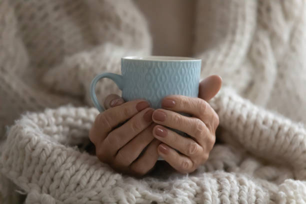 Close up mature woman wrapped warm blanket holding mug Close up mature woman wrapped warm blanket holding mug of coffee or tea, middle aged female enjoying free time, weekend at home, relaxing, drinking hot beverage in morning, starting new day sunday morning coffee stock pictures, royalty-free photos & images