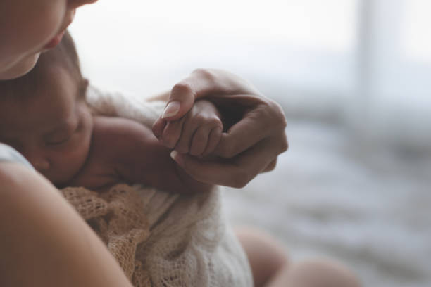 close up ibu berpegangan tangan bayi perempuan asia yang baru lahir dan sinar matahari di pagi hari. gadis kecil yang lucu berusia tiga minggu. kesehatan, perawatan, cinta, konsep hubungan. - memegang meraba potret stok, foto, & gambar bebas royalti