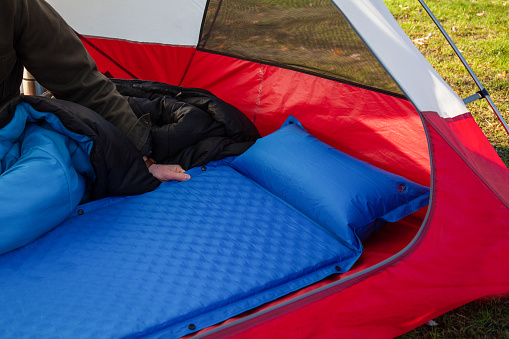 A man gets his tent and sleeping bag ready at a campground by inflating and setting up his blue blow-up mattress pad to put for under his sleeping bag